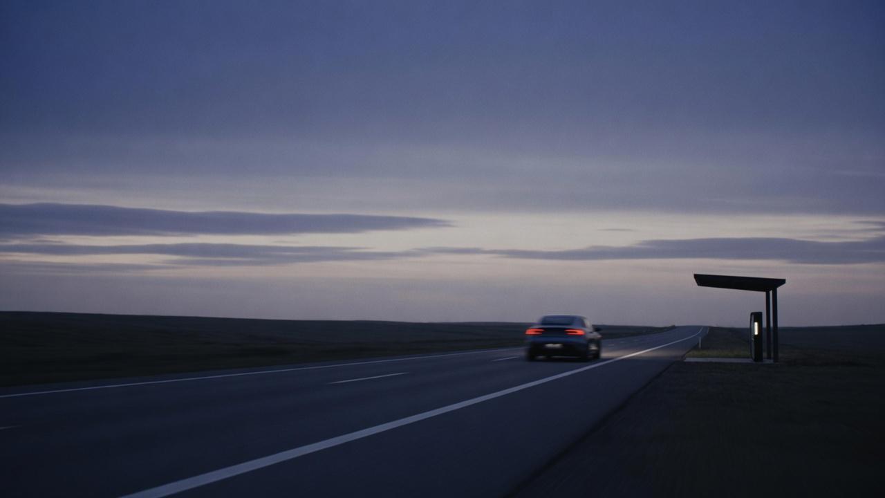 An EV on a highway at dusk beside a charging canopy